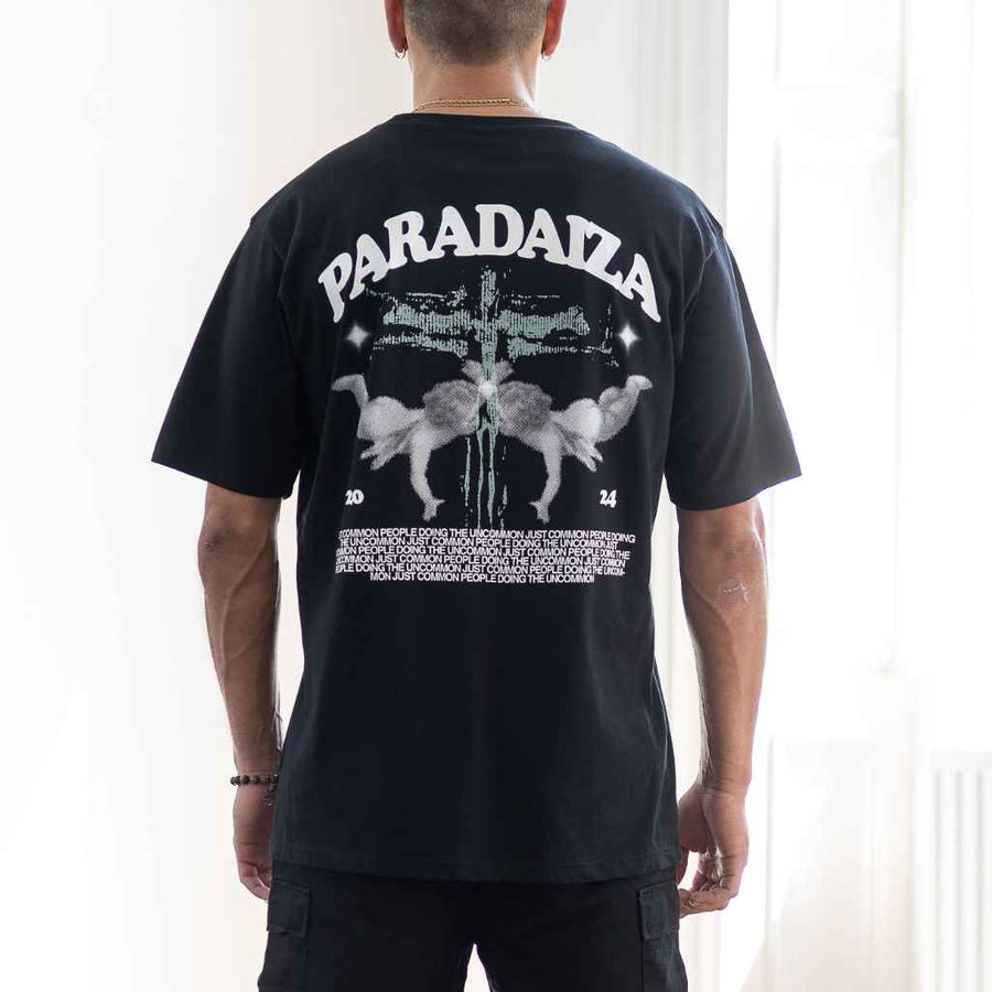 A person wearing para daiza  black oversized t-shirt with a graphic print on the back, the text 'PARADIZA' is prominently featured along with an illustrated motif.