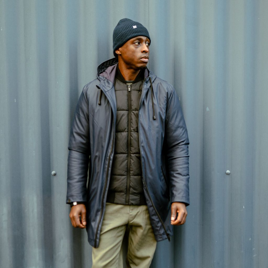 Man wearing a black paradaiza padded jacket and glasses standing on a street.