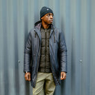 Man wearing a black paradaiza padded jacket and glasses standing on a street.