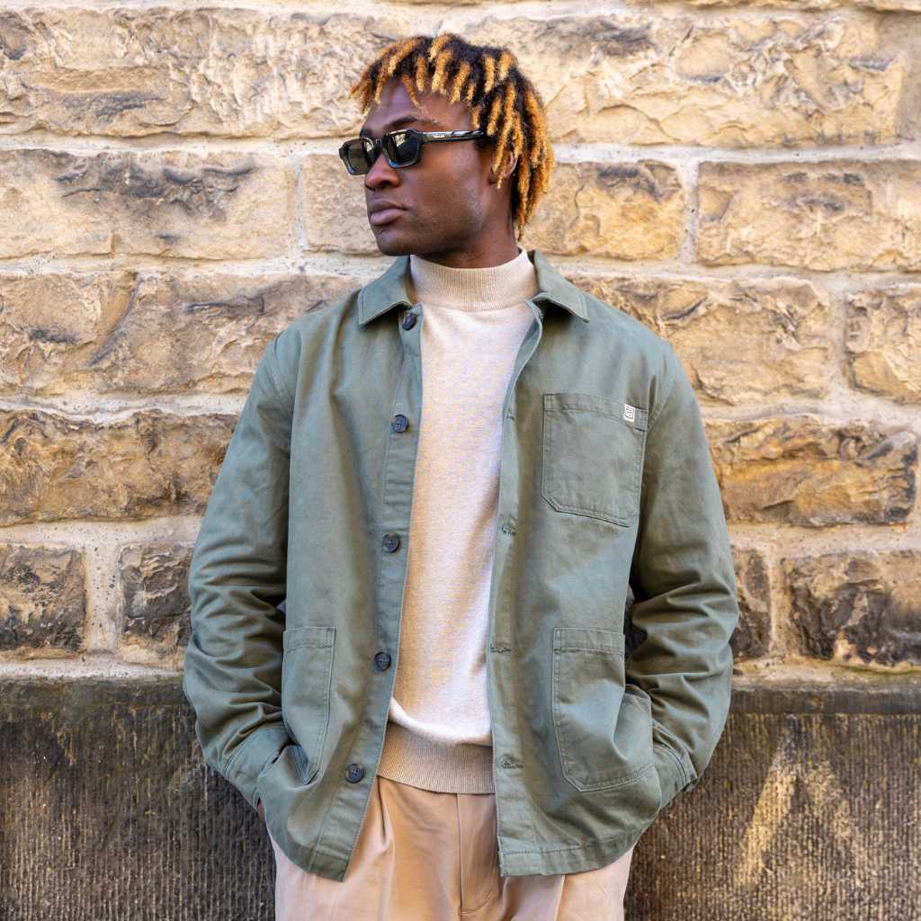 Man wearing a paradaiza worker jacket and sunglasses against a brick wall