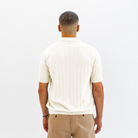 A man viewed from behind wearing a Paradaiza cream-colored short-sleeve polo shirt with vertical ribbed texture and tan trousers, set against a plain white studio background.