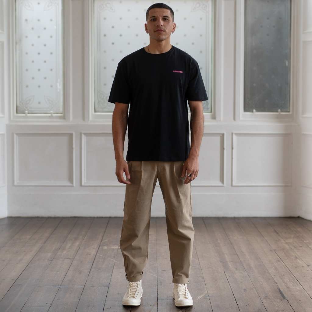 Man wearing a Paradaiza  black t-shirt with a small pink logo against a neutral background