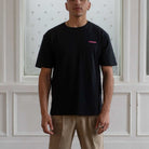 Man wearing a Paradaiza  black t-shirt with a small pink logo against a neutral background