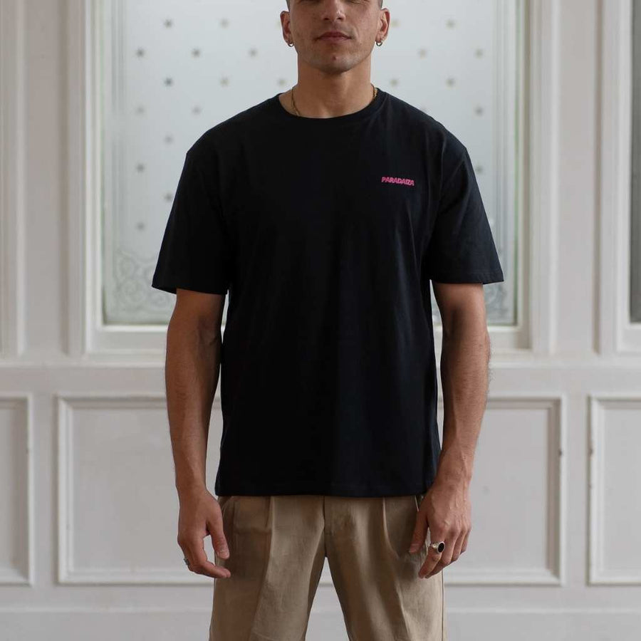 Man wearing a Paradaiza  black t-shirt with a small pink logo against a neutral background