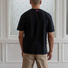 Man wearing a Paradaiza  black t-shirt with a small pink logo against a neutral background