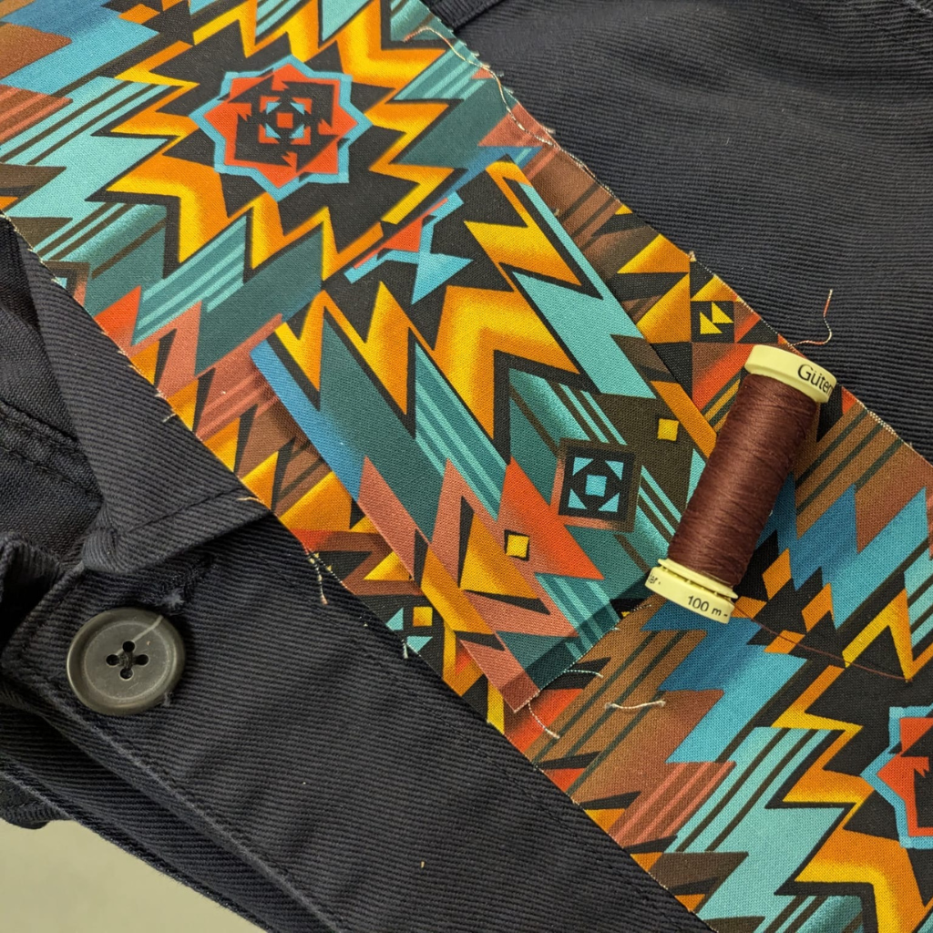Remode Collective thread spool on a colorful geometric-patterned fabric with navy PARA-DAIZA atelier jacket in the background