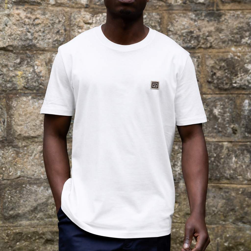 Person wearing a paradaiza white t-shirt with a small logo against a stone wall.