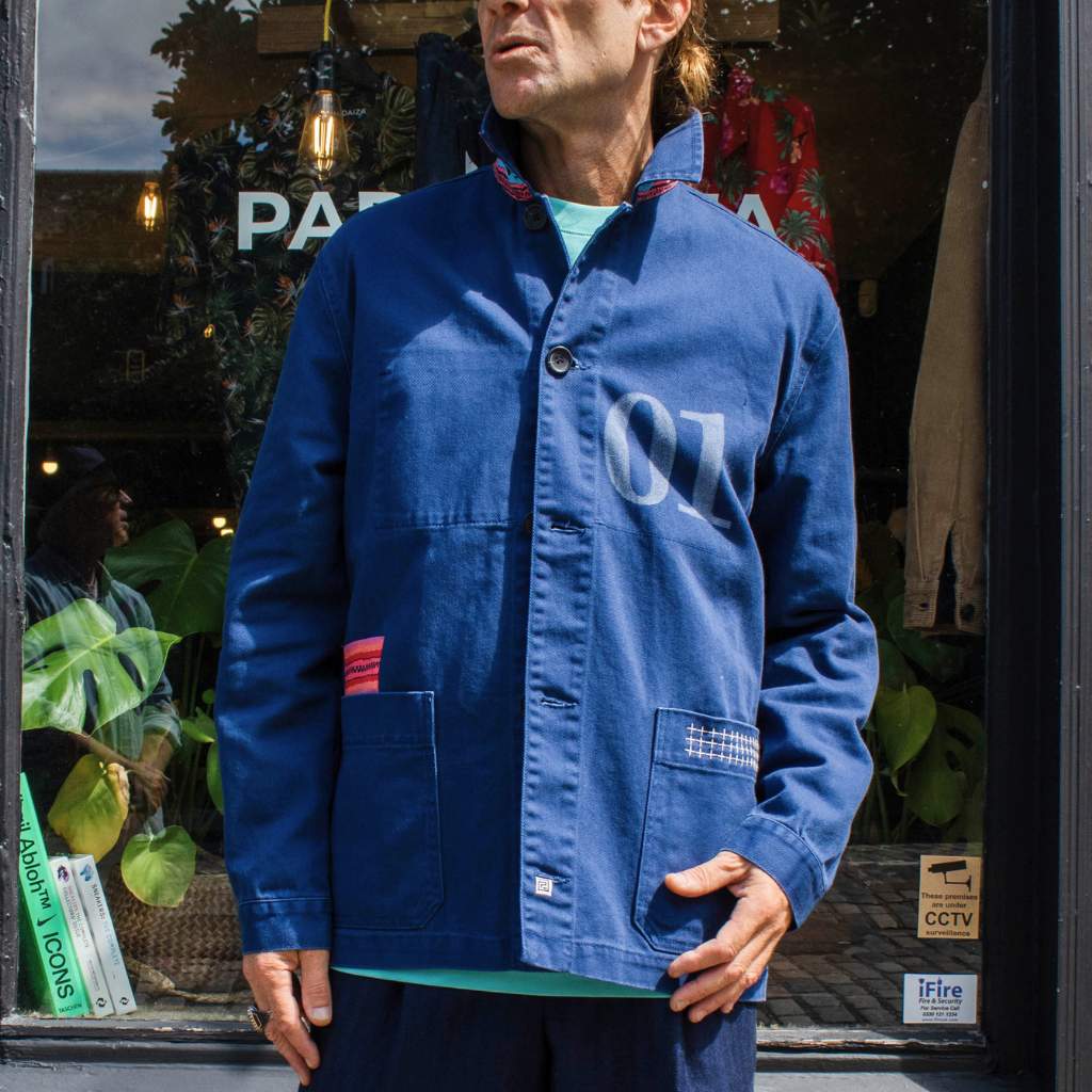 A person wearing a paradaiza blue atelier worker jacket with '01' printed on the chest, featuring a collar, button-up front, and two front patch pockets.