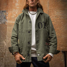 Man wearing a khaki jacket with '01' logo against a textured wall in Edinburgh.