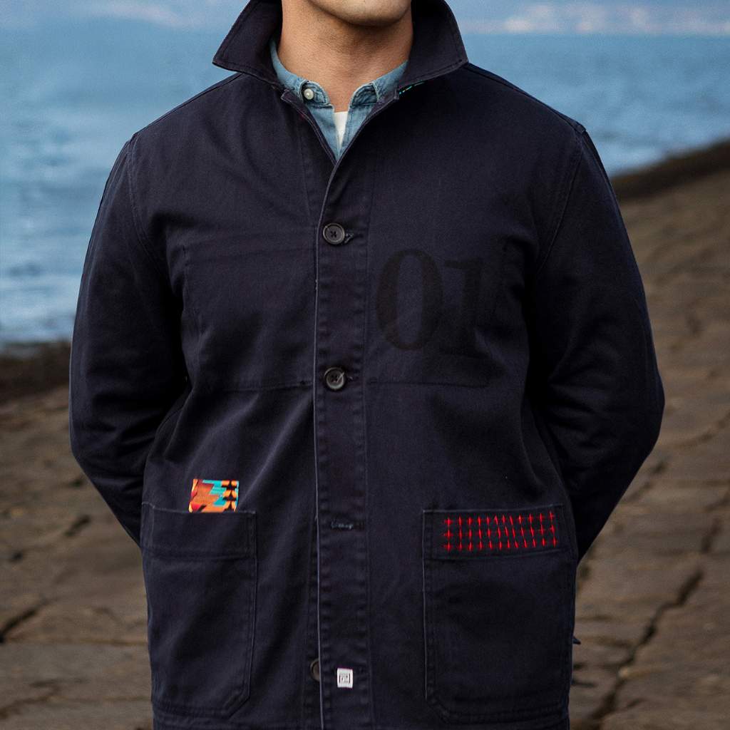 Person wearing a navy PARA-DAIZA navy jacket with colorful patches on a beach in Edinburgh.