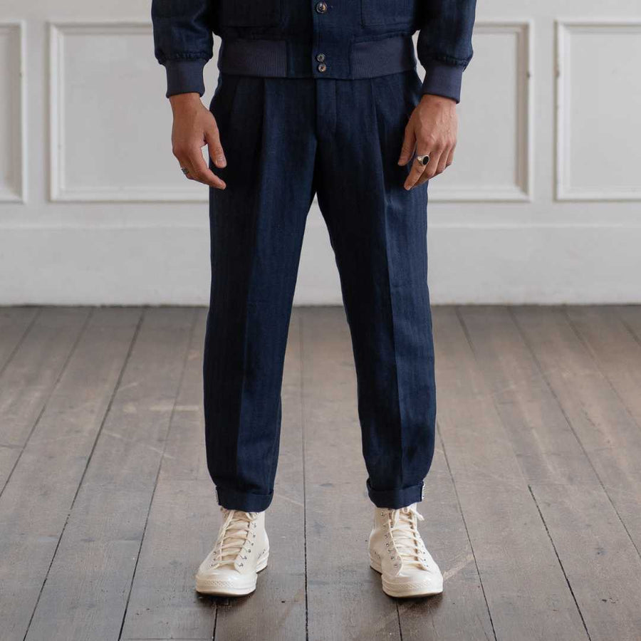 Person wearing a para daizannavy blue chinos with white sneakers on a wooden floor.