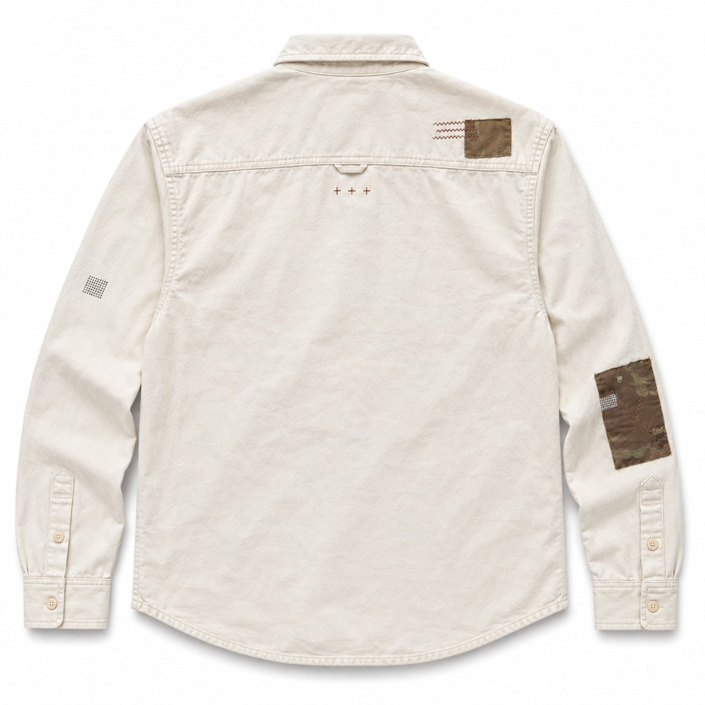 An off-white long-sleeve button-up shirt shown from the back, featuring brown camouflage patches on the upper back and one sleeve, and a small embroidered sashiko details 