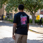 Person wearing a paradaiza black t-shirt with a graphic design on the back, standing outdoors.