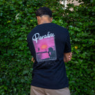Person wearing a black paradaiza t-shirt with 'Paradise' design against a green leafy background