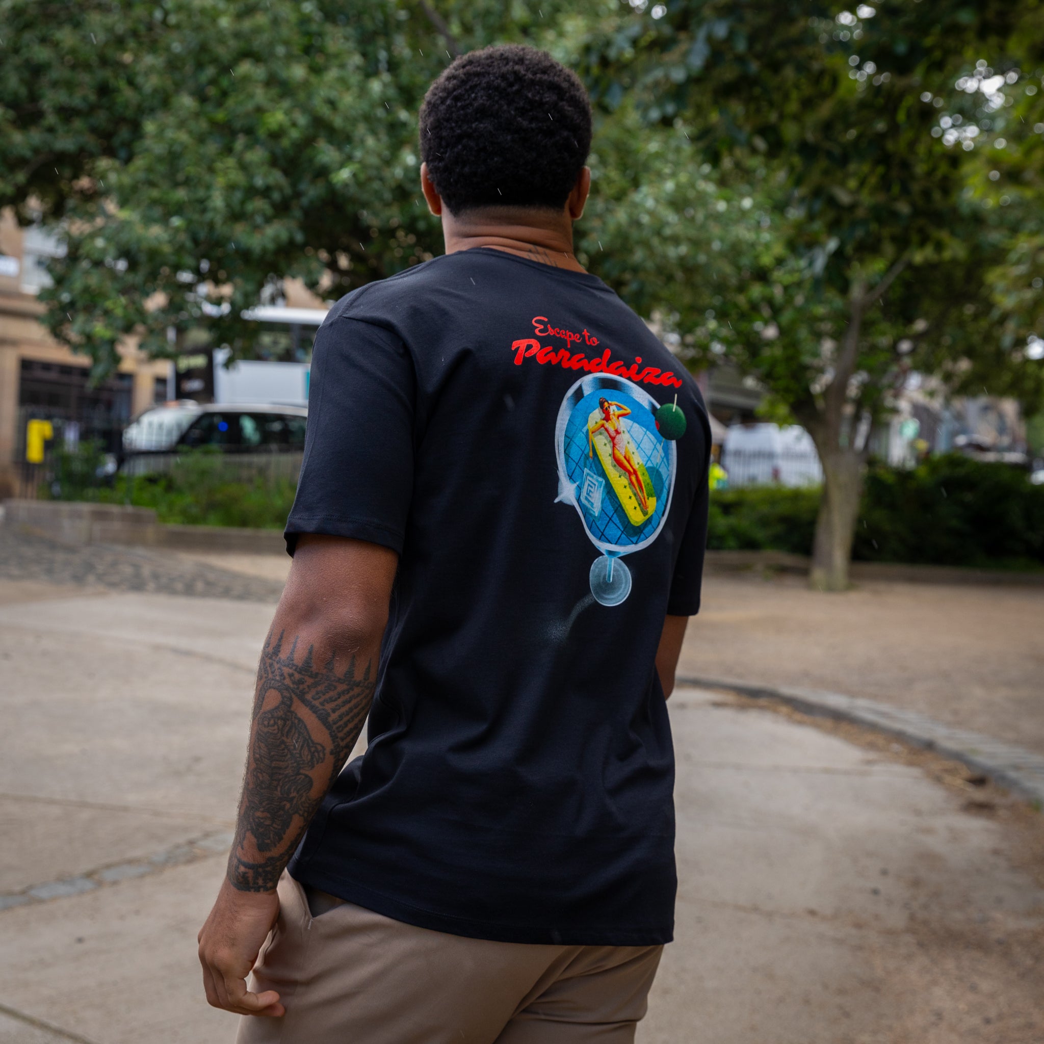 Person wearing a paradzia black t-shirt with a colorful graphic on the back, standing outdoors.
