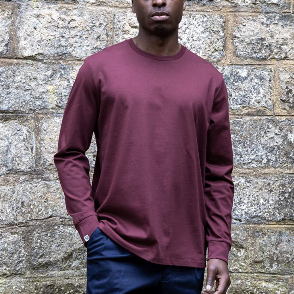 Person wearing a maroon paradaiza long-sleeve shirt against a stone wall.