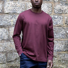 Person wearing a maroon paradaiza long-sleeve shirt against a stone wall.