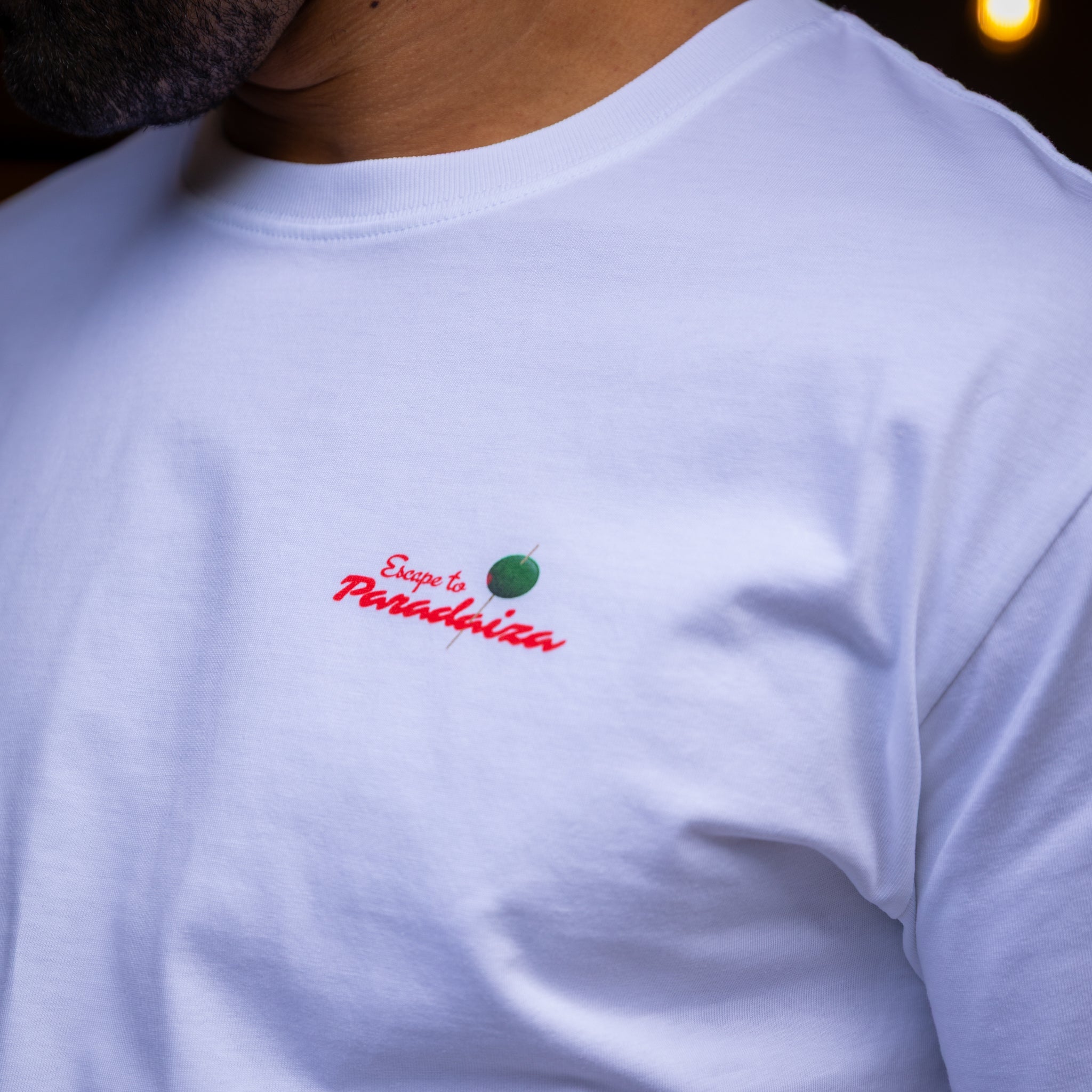 White t-shirt with 'Escape to Paradise' text and logo on a dark background