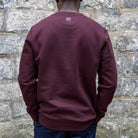Person wearing a paradaiza maroon sweatshirt against a stone wall background