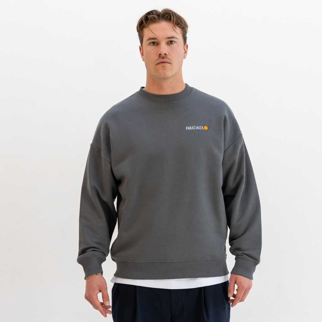 Man wearing a grey paradaiza sweatshirt with a logo on a white background