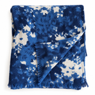 A folded throw blanket featuring a blue and off-white tie-dye pattern with fringed edges, displayed on a clean white background.