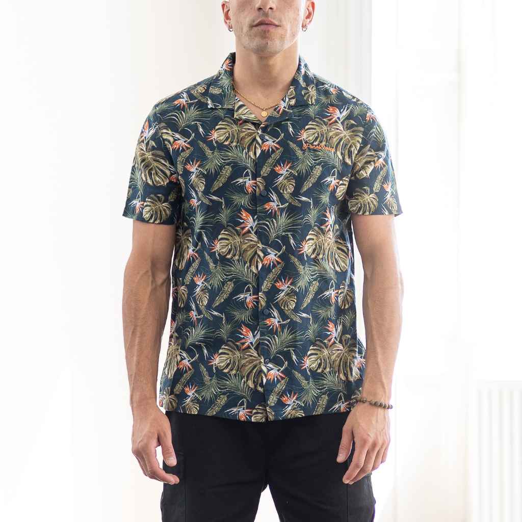 model wears paradaiza  Paradise Print Shirt is made from a blend of 62% linen and 38% organic cotton, creating a lightweight and breathable fabric. The slim/regular fit with a classic bowling neck and self coloured button