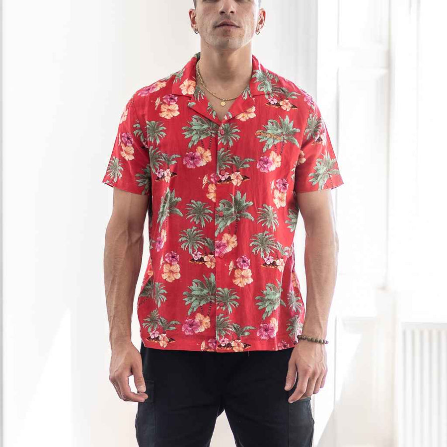 Model wears a red Paradise Print Shirt is made from a blend of 62% linen and 38% organic cotton, creating a lightweight and breathable fabric. The slim/regular fit and classic bowling neck with self coloured buttons. 