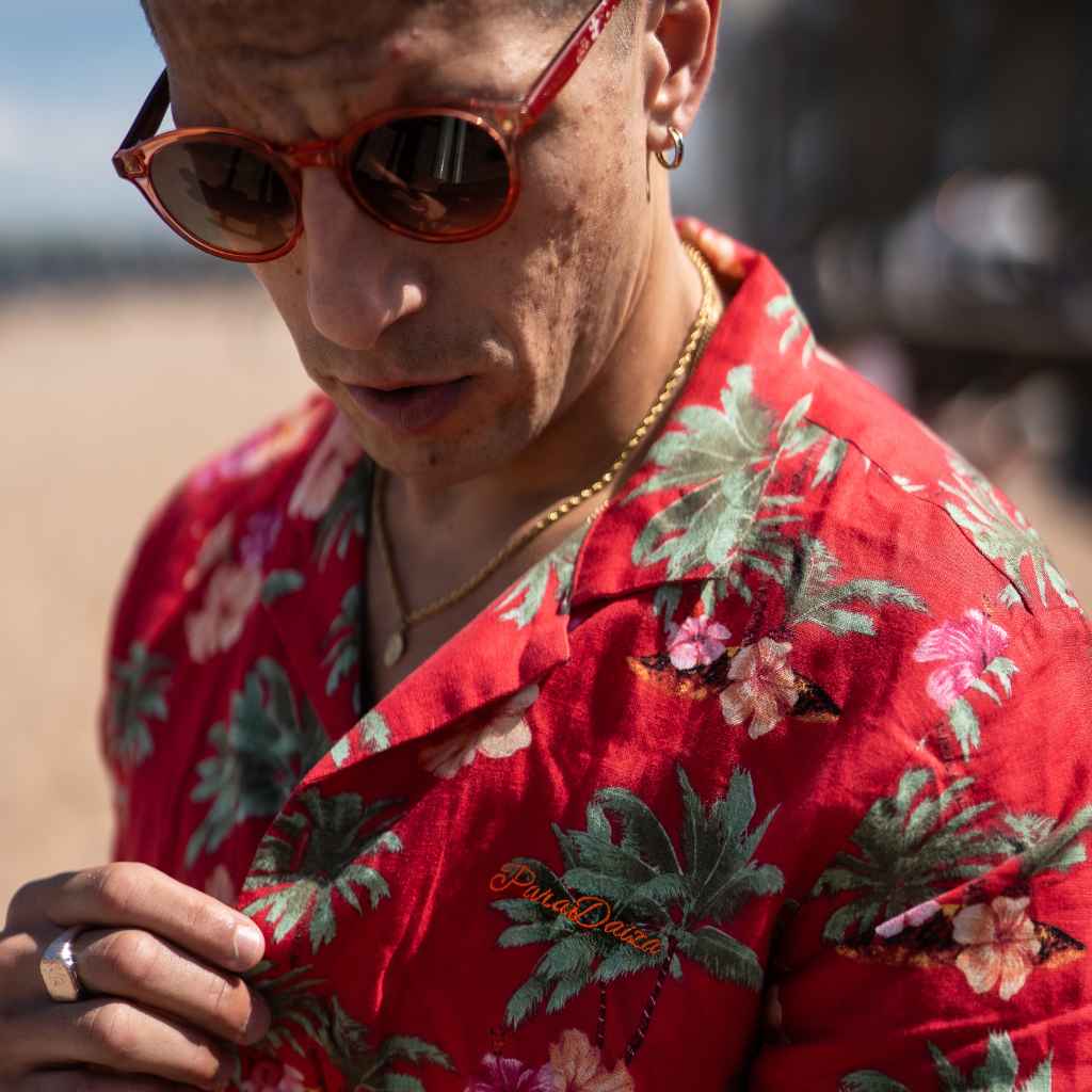 Model wears red Paradise Print Shirt is made from a blend of 62% linen and 38% organic cotton, creating a lightweight and breathable fabric. The slim/regular fit and classic bowling neck with self coloured buttons