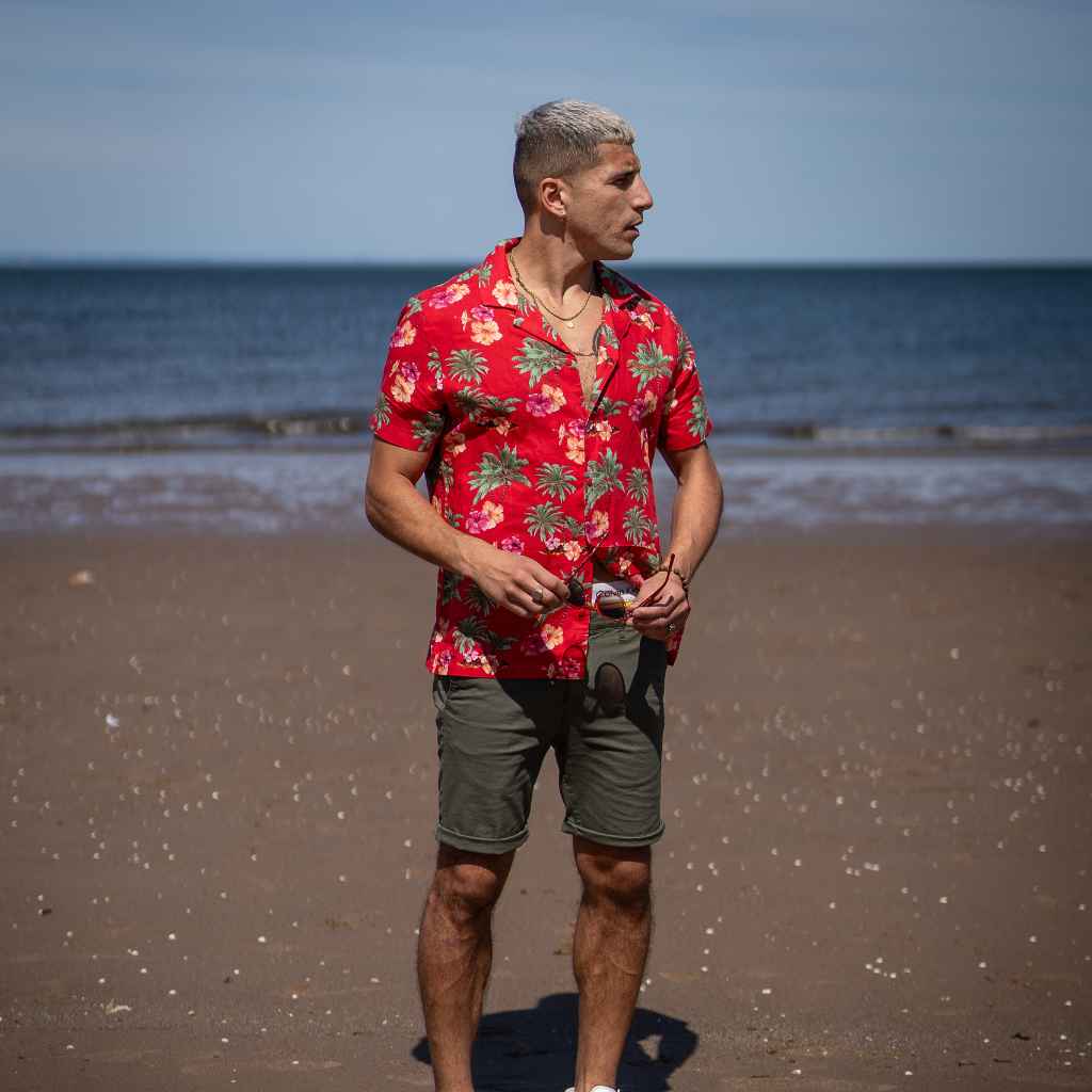 Model wears red Paradise Print Shirt in red  and khaki shorts at the beach