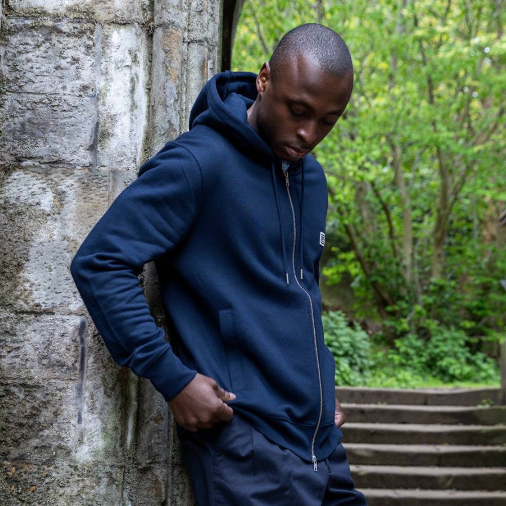 Man wearing a navy paradaiza hoodie with a brand logo, standing in front of a store window.
