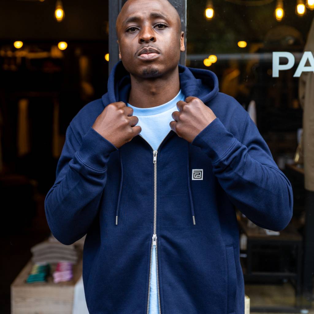 Man wearing a navy paradaiza hoodie with a brand logo, standing in front of a store window.