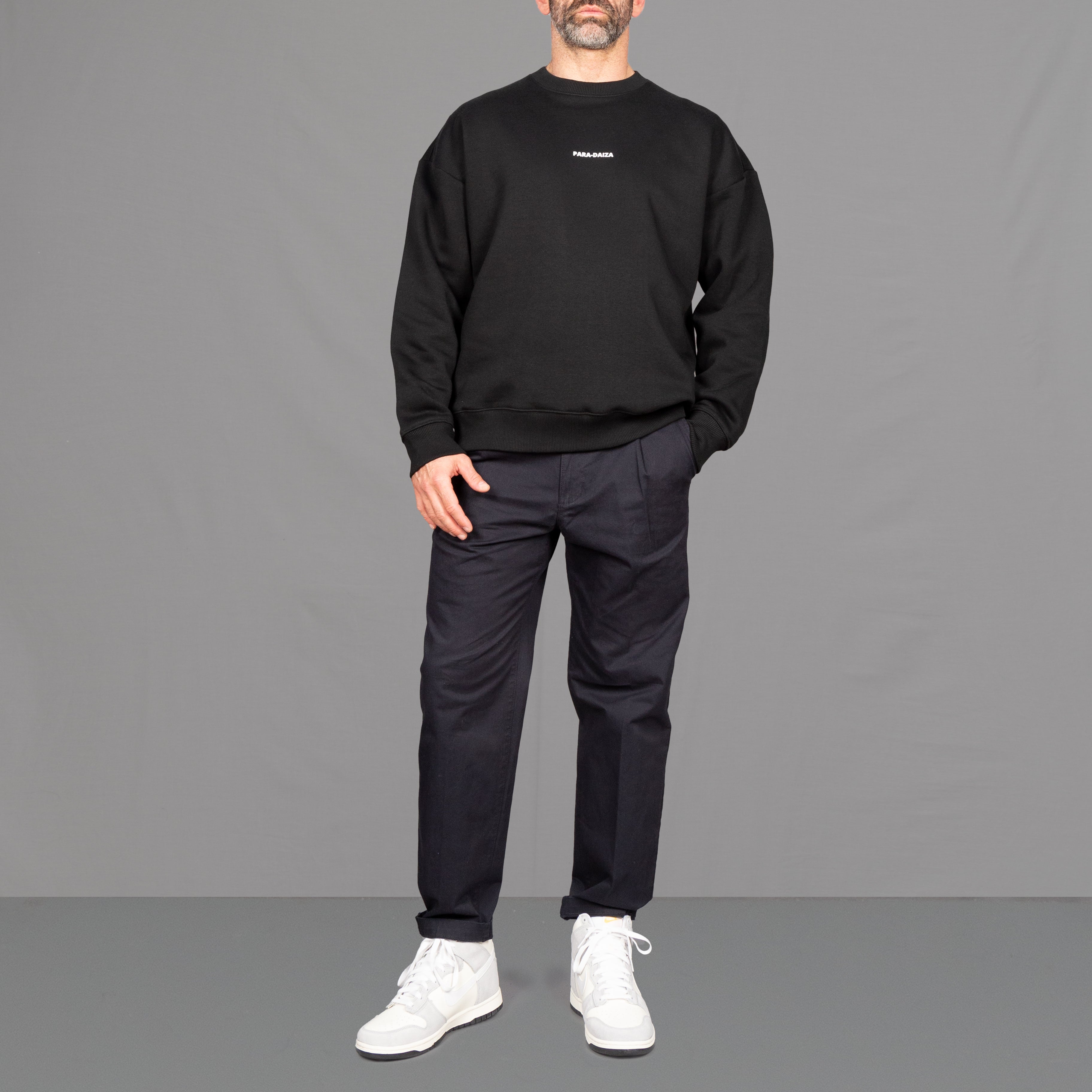 model wears a black sweatshirt with navy chinos