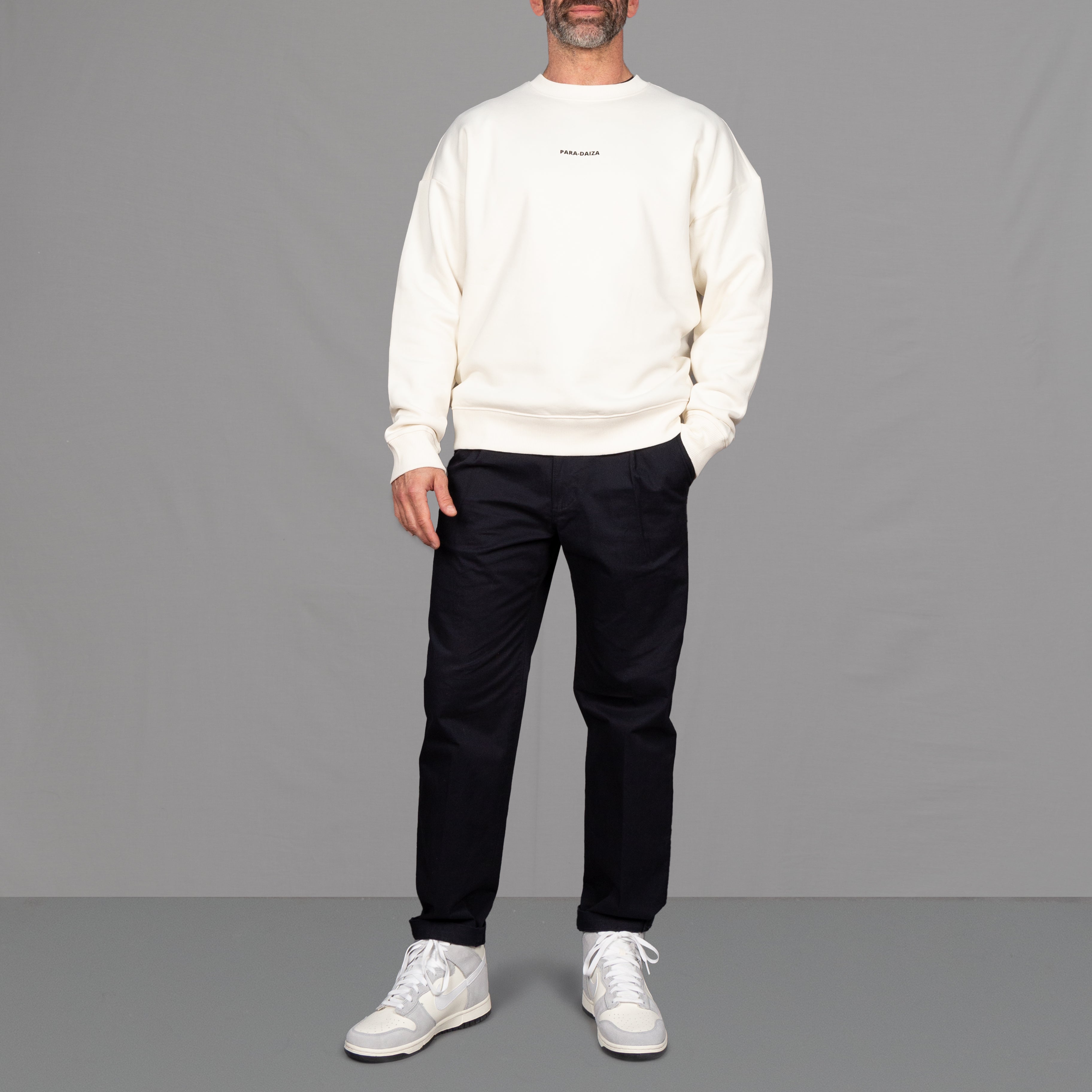 model wears a white sweatshirt with navy chinos