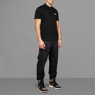 The model wears Para-Daiza Black Core Polo Shirt, pinch chino and Nike trainers.