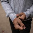 Close-up of a person wearing a gray sweater with a brand logo on the sleeve.