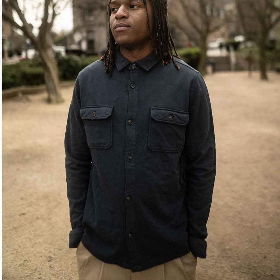 A person standing outdoors wearing a navy cotton soft overshirt with long sleeves, two chest pockets, and button closures.
