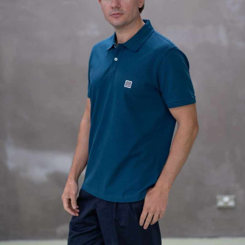 Man wearing a blue polo shirt with a logo against a gray wall