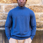 Man wearing a blue paradaiza highneck sweater against a stone wall