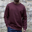 Person wearing a paradaiza maroon sweatshirt against a stone wall background