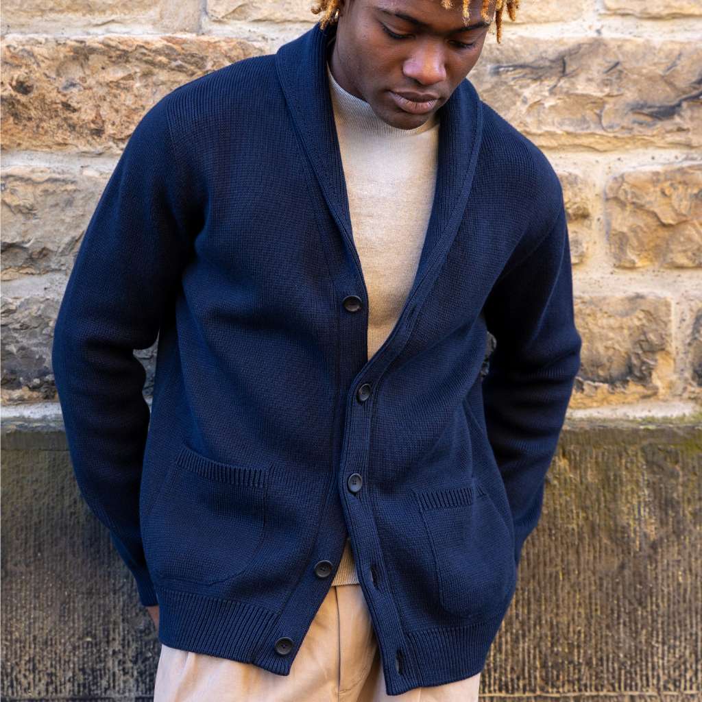 Person wearing a paradaiza navy blue cardigan over a beige shirt against a stone wall.
