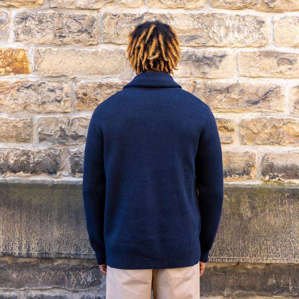Person wearing a paradaiza navy blue cardigan over a beige shirt against a stone wall.