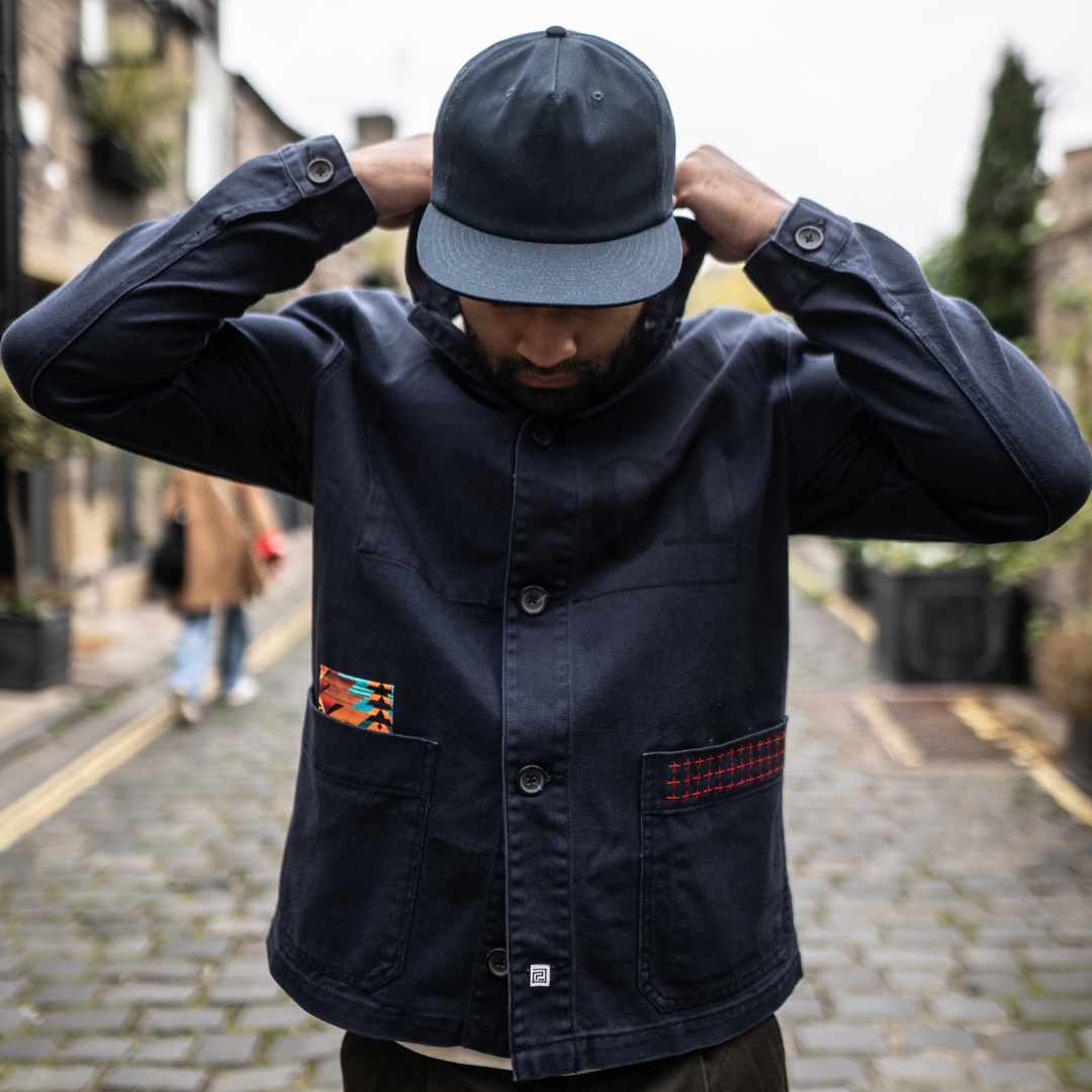 Model wearing a  paradaiza dark blue worker jacket with patterned accents and sashiko stitching  in a studio.