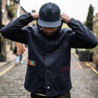 Model wearing a  paradaiza dark blue worker jacket with patterned accents and sashiko stitching  in a studio.