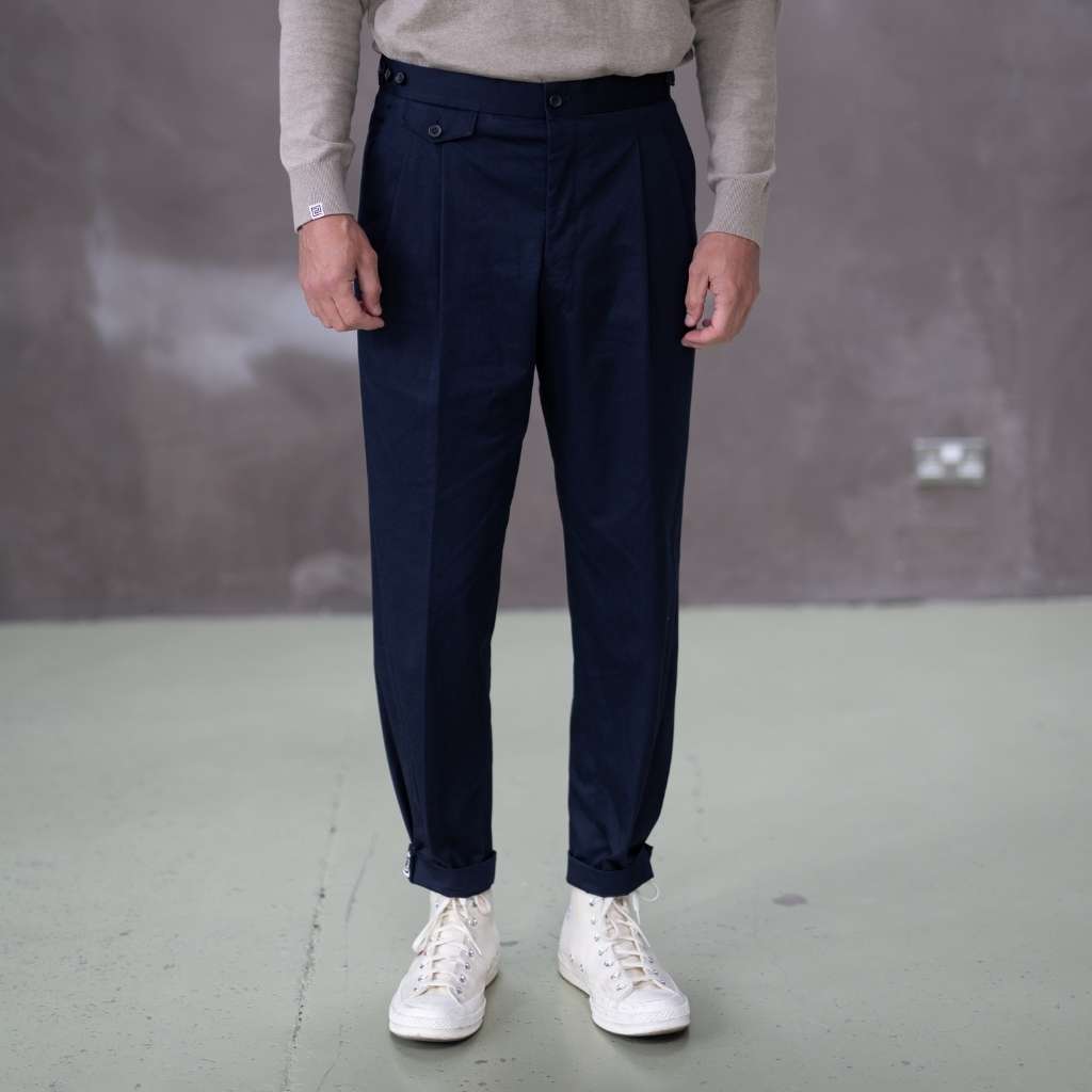 Person wearing paradaiza navy pinch chinoa pants and white sneakers with red heart design on a gray floor.