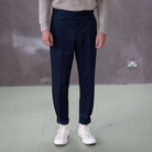 Person wearing paradaiza navy pinch chinoa pants and white sneakers with red heart design on a gray floor.