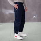 Person wearing paradaiza navy pinch chinoa pants and white sneakers with red heart design on a gray floor.