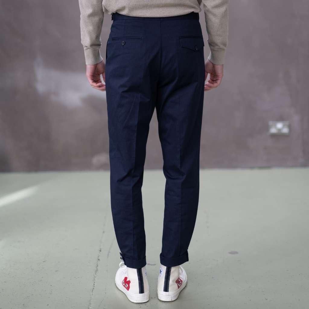 Person wearing paradaiza navy pinch chinoa pants and white sneakers with red heart design on a gray floor.