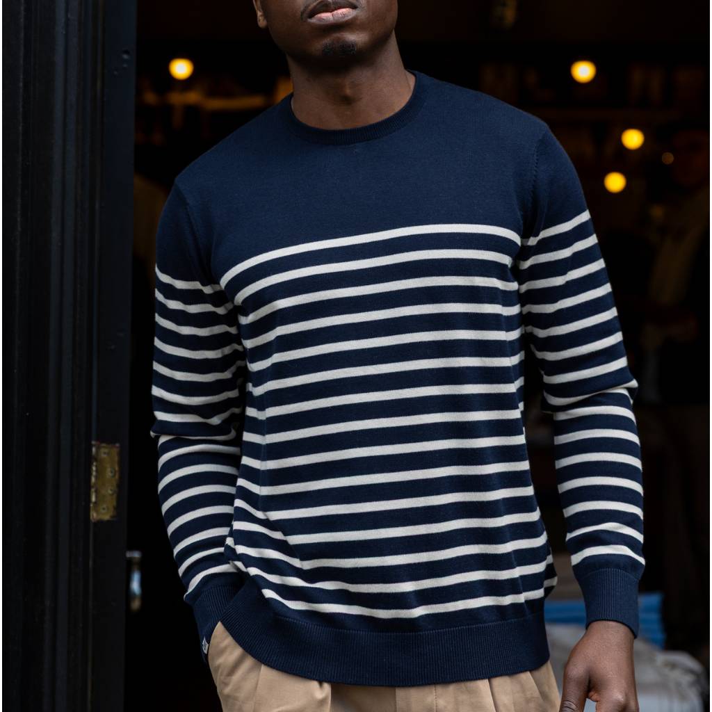 Person wearing a navy and white paradaiza striped sweater against a dark background
