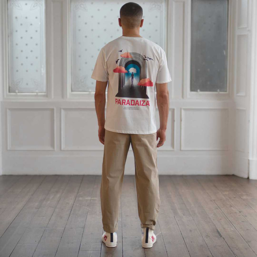 Person wearing a white t-shirt with a graphic design and 'Paradaiza' text, standing in a room with wooden flooring and white paneled walls.