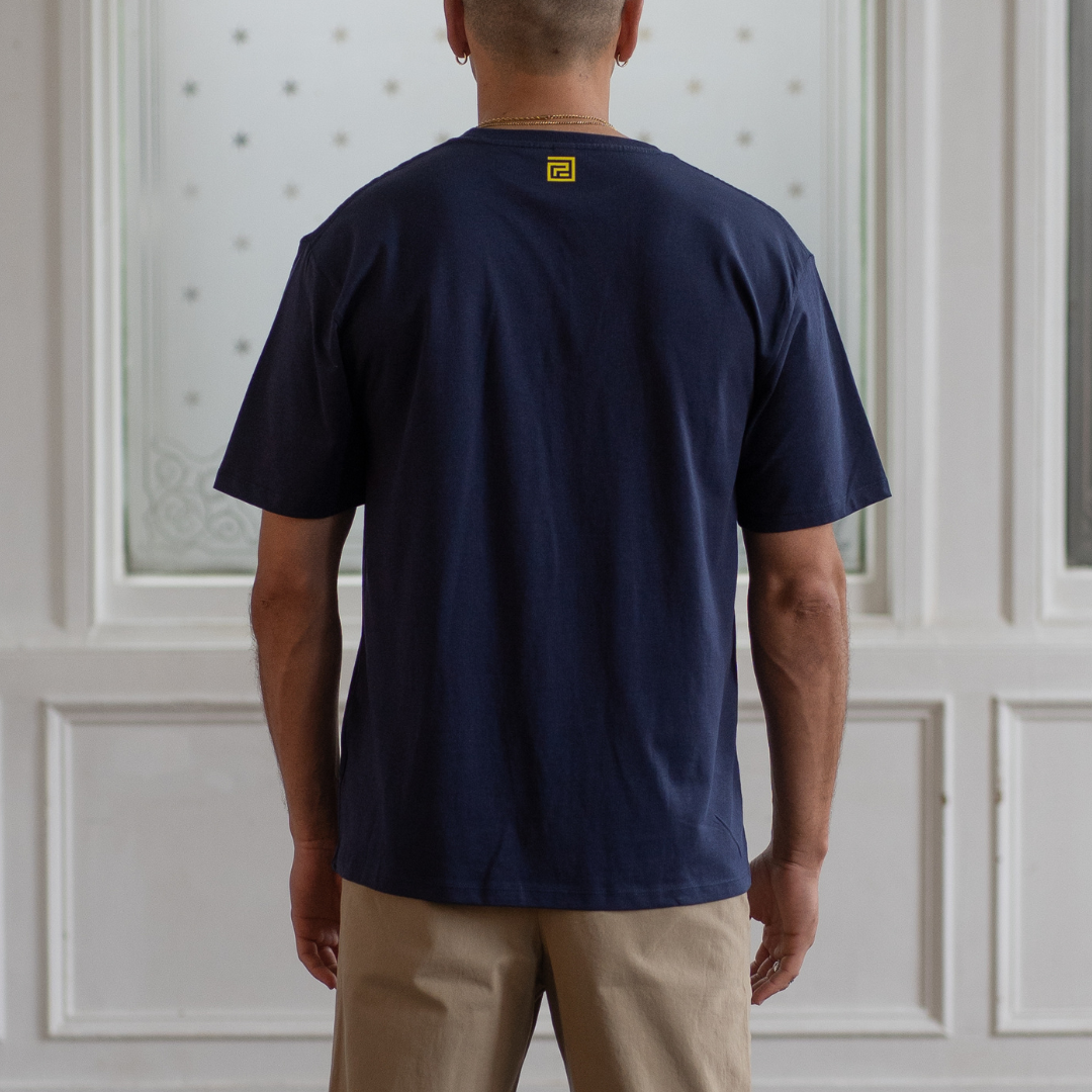 model  wearing a  paradaiza navy blue t-shirt with a  yellow logo in front of a white paneled wall.
